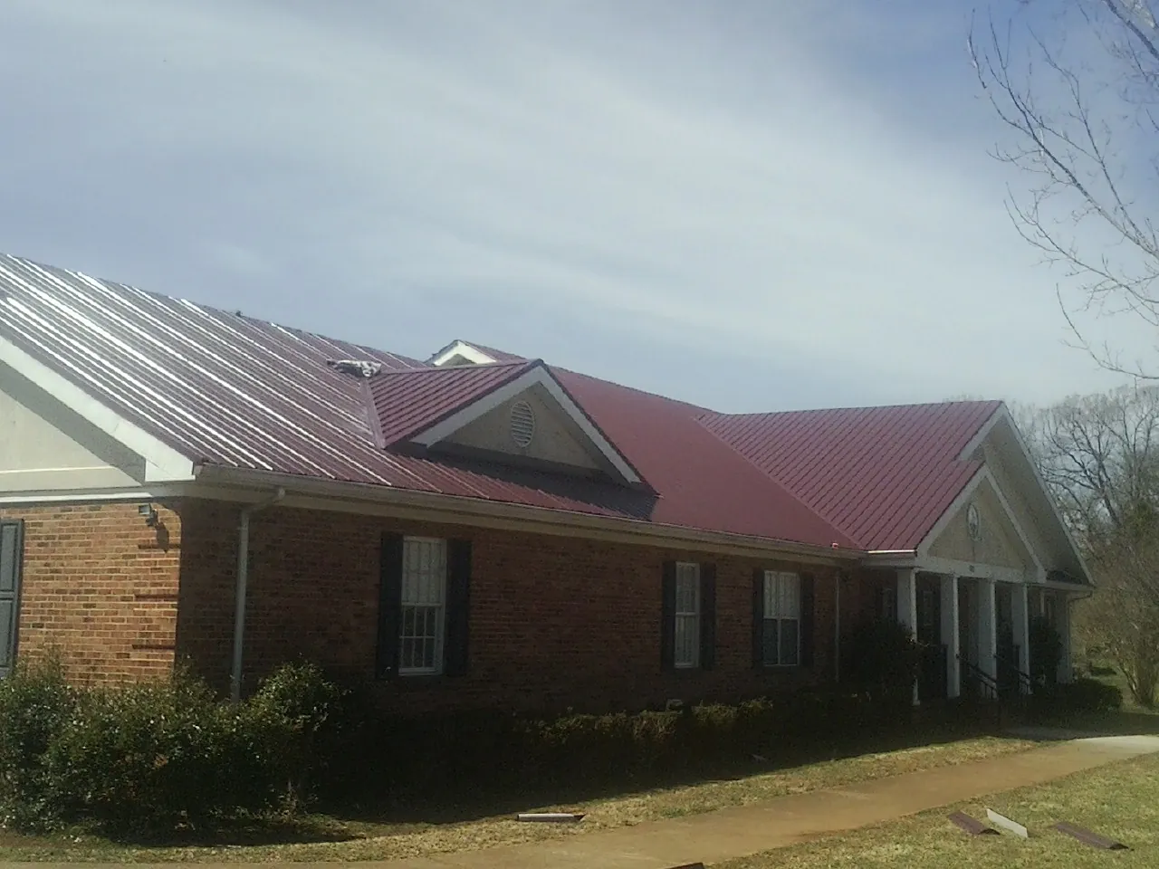 Red metal roof with gabled entries on a long brick building, from a Hail Damage Roof Repair job in Allendale
