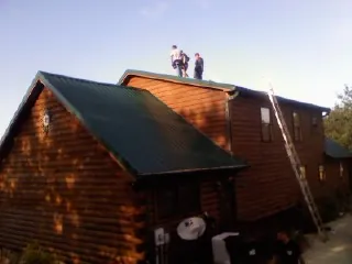 Crew on the ridge of a green metal roof on a two story log home in Allendale