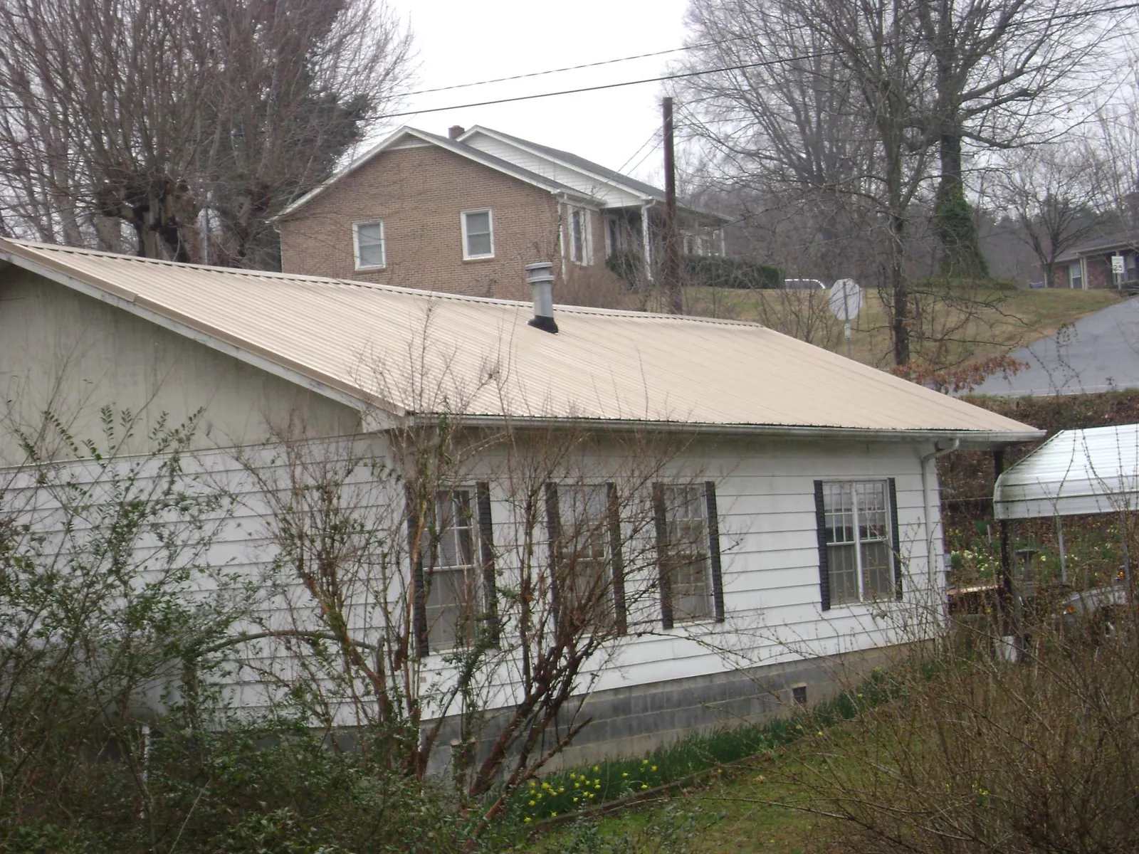 Tan metal roof on a white sided house set into a hillside — Commercial Roofing by Roofing Brothers in Allendale