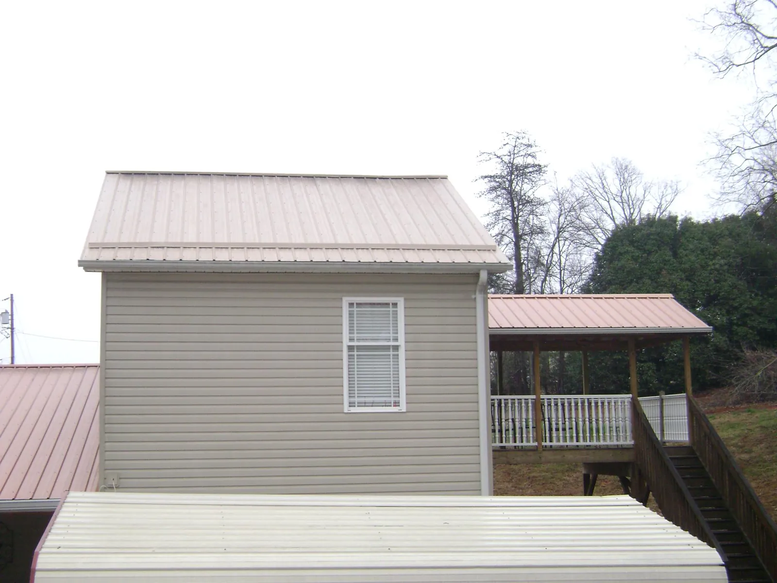 Tan metal roofs on a two story addition and attached porch, from a Roof Replacement job in Allendale